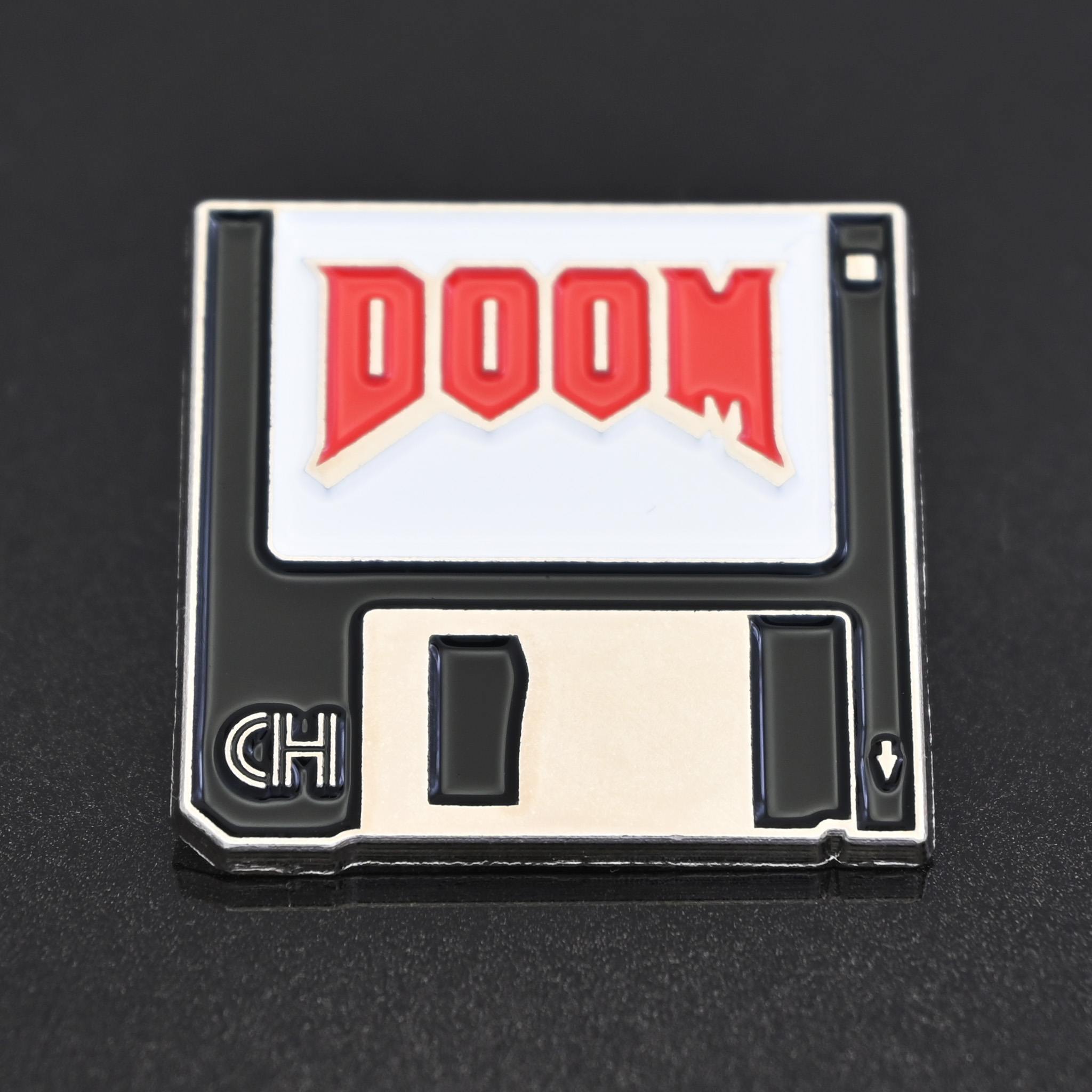 A disk shaped enamel pin with the 90s DOOM video game logo on the diskette