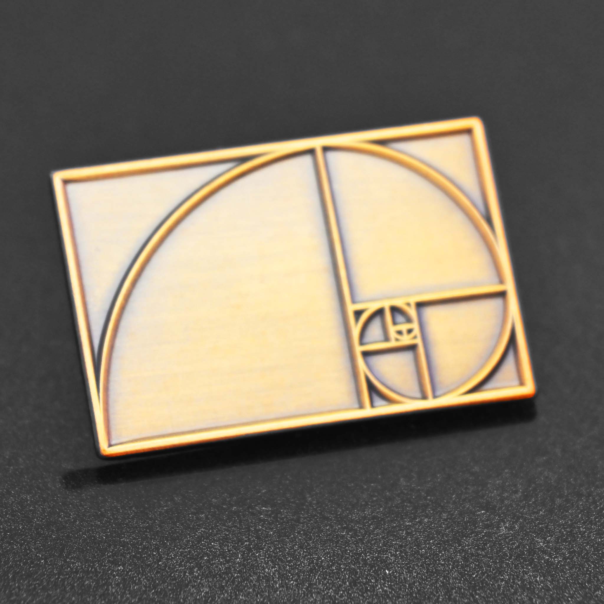 An antique brass enamel pin featuring the Golden Ratio - perfect for designers and artists