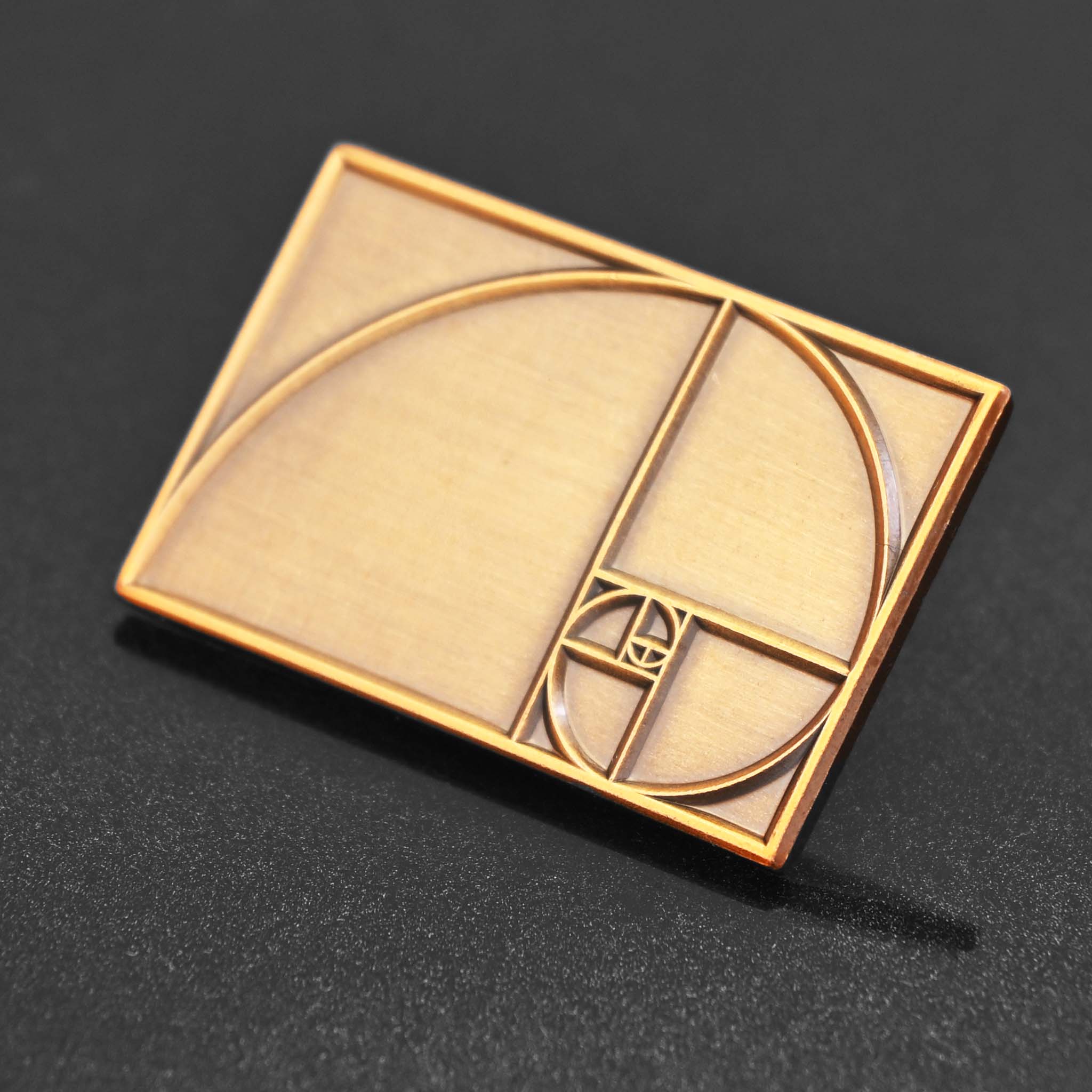An antique brass enamel pin featuring the Golden Ratio - perfect for designers and artists
